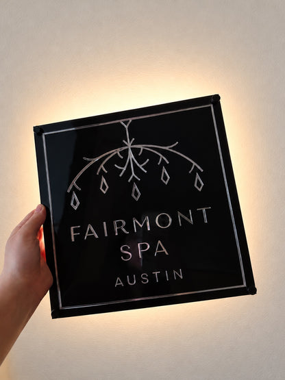Black layered acrylic Fairmont Spa logo sign with reflective lettering and warm backlighting.