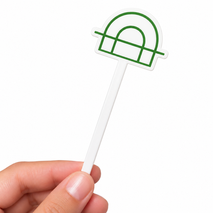 A hand holding a white plastic cocktail pick or party pick decorated with a green arch graphic outline, set against a plain white background.