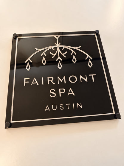 Front view of a black square acrylic business logo sign with reflective decorative details and lettering.