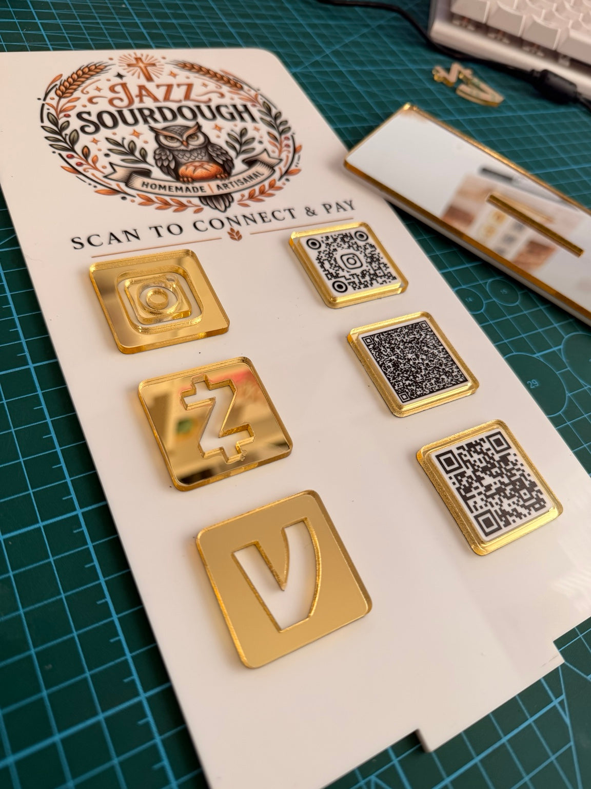Original close-up photograph of layered gold mirror details and three QR codes on a white acrylic business sign.