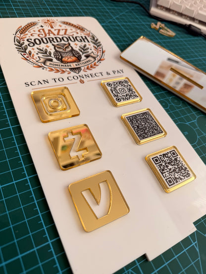 Original close-up photograph of layered gold mirror details and three QR codes on a white acrylic business sign.