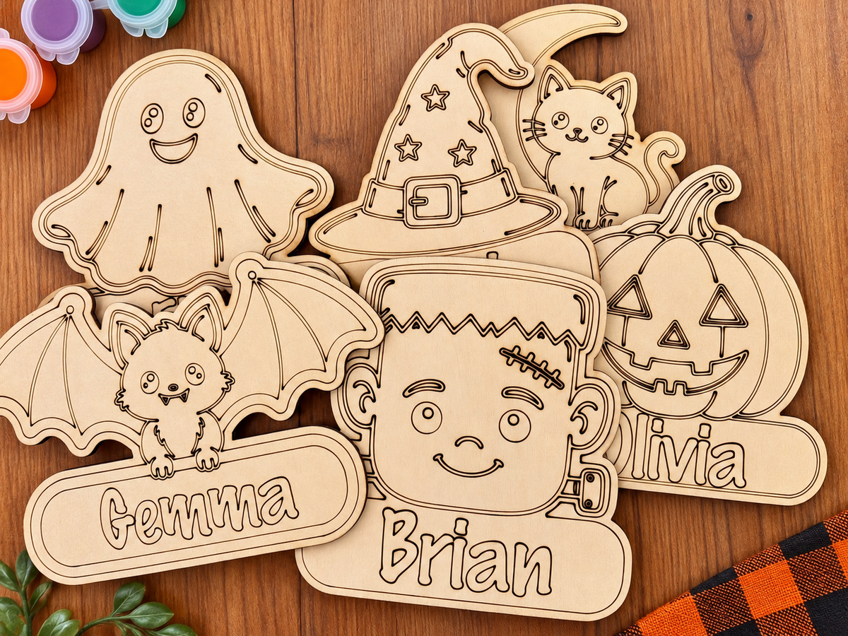 A set of personalized wooden laser-cut Halloween decorations, including a bat, ghost, witch hat, jack-o'-lantern, cat, and names like Emma, Brian, and Olivia, arranged on a wooden tabletop.