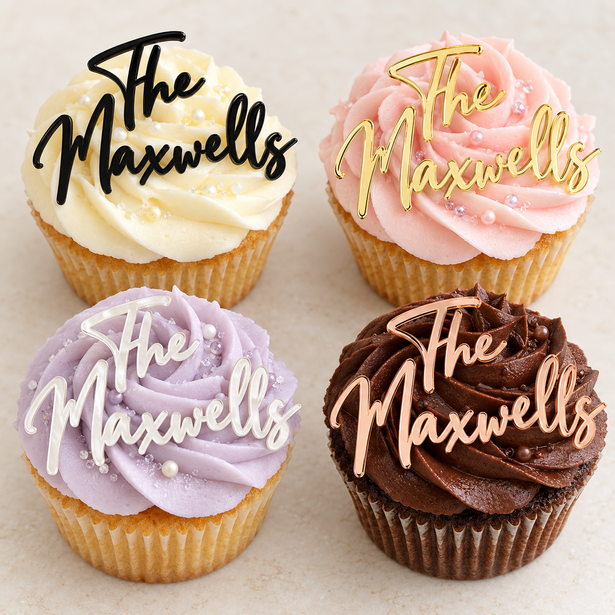 Four cupcakes with ivory, pink, lavender and chocolate icing, each displaying a “The Maxwells” acrylic name charm in black, gold, white or rose gold.