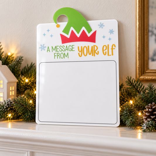 Blank acrylic elf Christmas dry-erase message board leaning on a mantel with festive greenery.