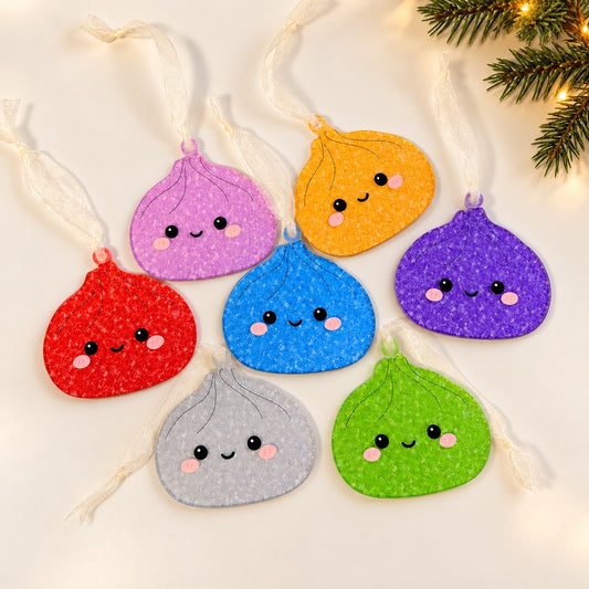 Seven glitter dumpling acrylic ornaments in Pink, Red, Purple, Gold, Blue, Green and Silver with sheer hanging ribbons on an ivory holiday backdrop.
