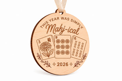 Round engraved wood mahjong Christmas ornament reading This year was simply Mahj-ical 2026, with three tile designs and beige ribbon.