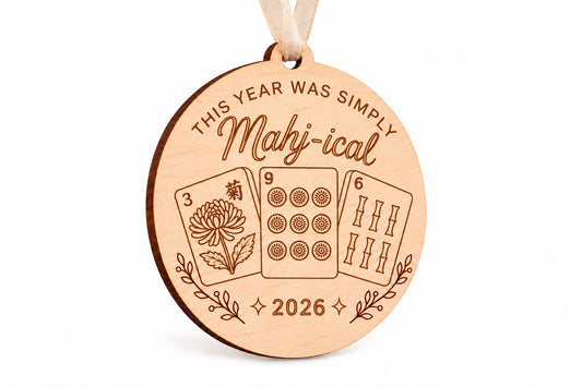 Round engraved wood mahjong Christmas ornament reading This year was simply Mahj-ical 2026, with three tile designs and beige ribbon.