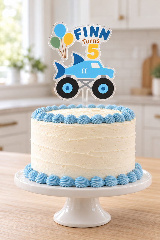 Personalized blue shark monster truck cake topper with Finn name and age 5 on a white birthday cake with blue piping