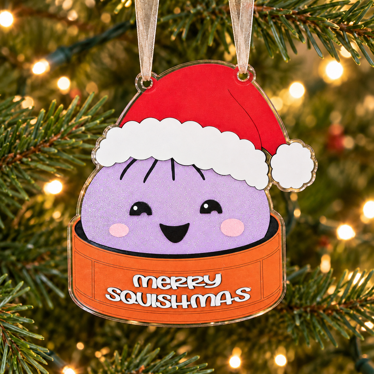 Light purple glitter merry squishmas UV printed acrylic Christmas ornament hanging on a Christmas tree, with sheer beige ribbon.